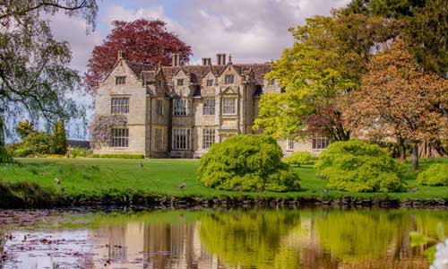 An old building at Wakehurst with water in front of it and some trees